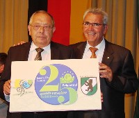 Bürgermeister Georg Lettner und Bürgemeister Jean-Paul Monin halten ein Bild mit bei Logos der Gemeinden drauf