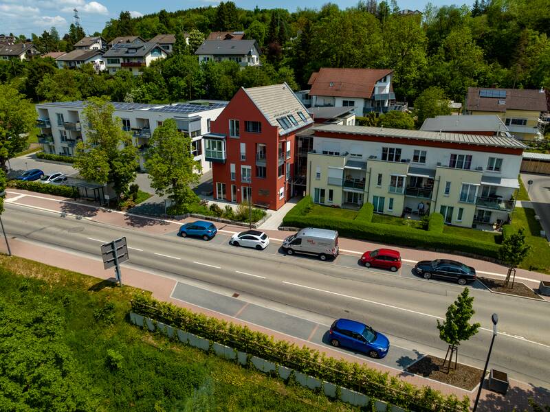 Die Aufnahme zeigt eine Wohnstraße mit mehreren modernen Gebäuden des Seniorenzentrums mit geparkten Autos entlang der Straße und viel Grün im Hintergrund.