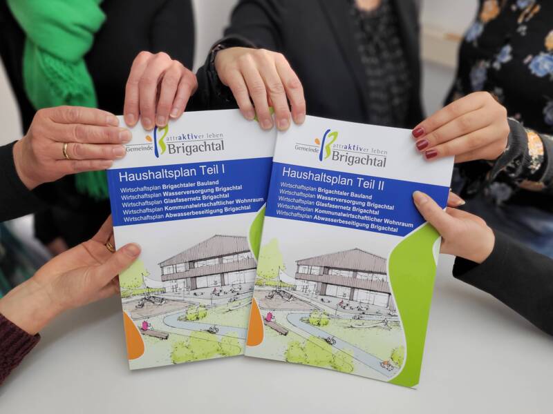 Mehrere Hände halten zwei Broschüren der Gemeinde Brigachtal mit dem Titel "Haushaltsplan Teil I" und "Haushaltsplan Teil II", die ein Gebäude und Landschaft darstellen.