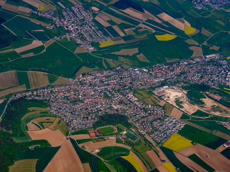 Das Bild zeigt eine Luftaufnahme von Brigachtal, umgeben von zahlreichen landwirtschaftlich genutzten Feldern in verschiedenen Farben und Mustern.