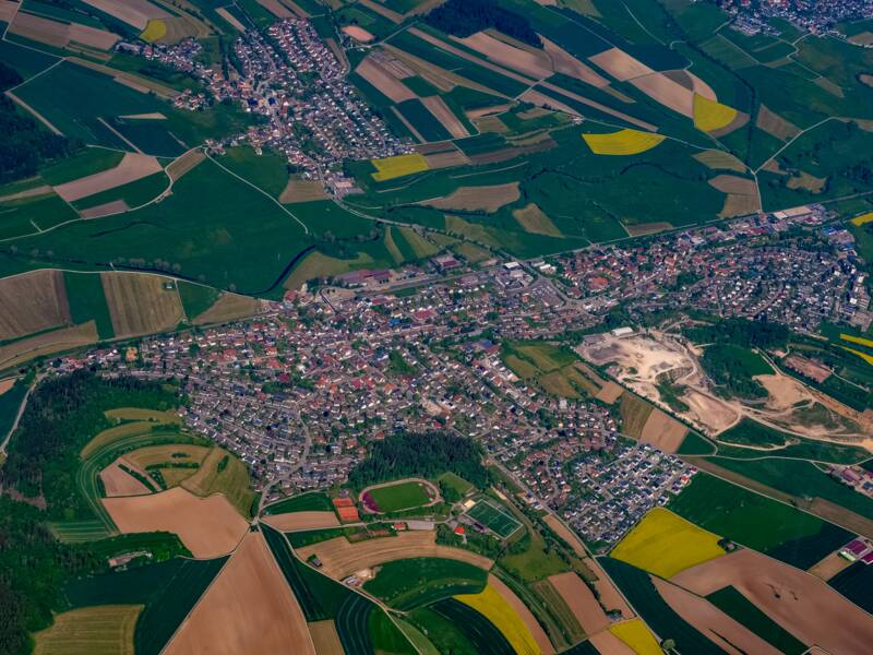 Das Bild zeigt eine Luftaufnahme von Brigachtal, umgeben von zahlreichen landwirtschaftlich genutzten Feldern in verschiedenen Farben und Mustern.