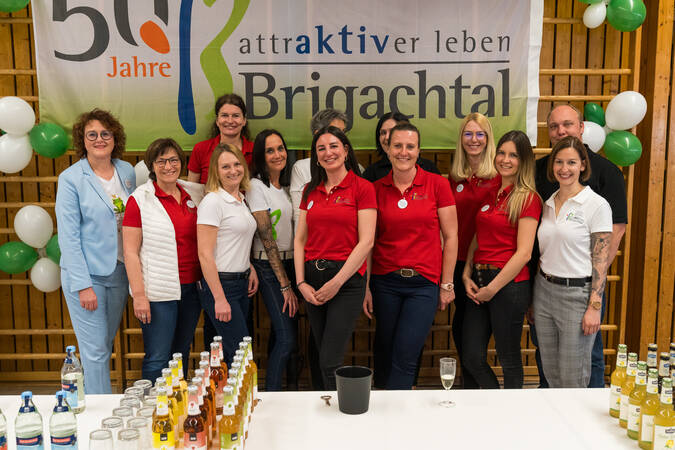 Eine Gruppe von Mitarbeitern steht vor einem Banner, das "50 Jahre Brigachtal" feiert, während im Vordergrund ein Tisch mit Getränken steht.