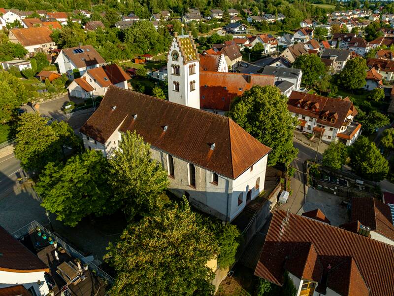 Luftaufnahme einer Kirche St. Martin  mit weißer Fassade und rotem Dach, eingebettet in eine ländliche Ortschaft mit grünen Bäumen und traditionellen Häusern bei Tageslicht.