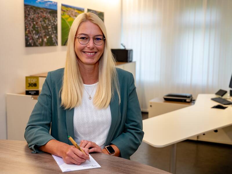 Katja Seng steht lächelnd an einer Theke in einem Büro und schreibt auf einem Notizblock.