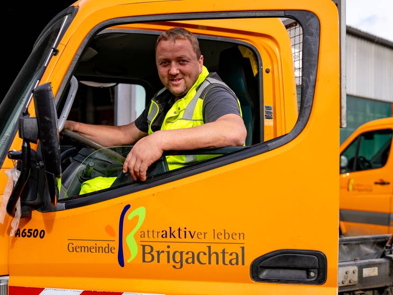 Günter Obergfellin einer Warnweste sitzt lächelnd  in der Fahrerkabine eines gelben Fahrzeugs, das mit dem Logo "Gemeinde Brigachtal" versehen ist.
