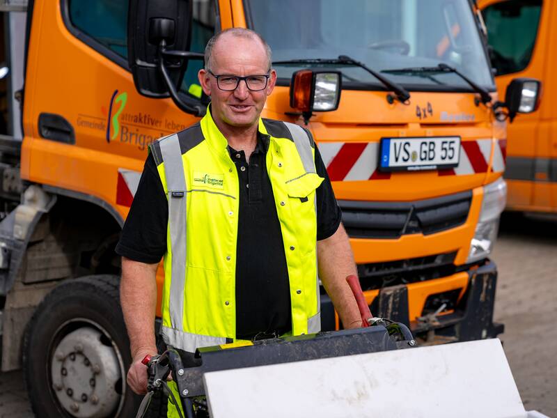 Uwe Seng mit einer gelben Warnweste steht vor einem orangefarbenen Lastwagen.