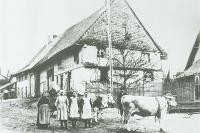 Im Hintergrund steht ein Bauernhaus, im Vordergrund eine Bauernfamilie mit Kühen