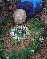 Auf dem Boden liegt ein Mandalbild aus Blättern und Blumen und ein Kind schaut es an